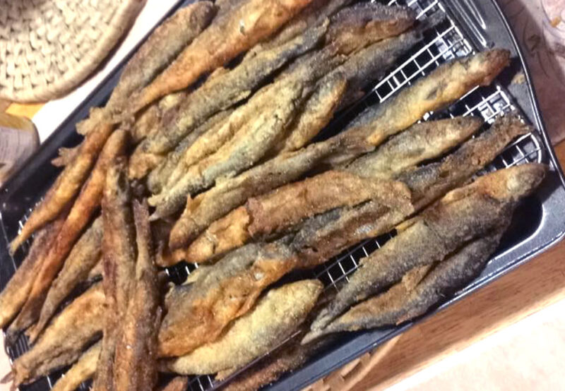A tray of golden-brown fried fish laid out on a cooling rack in a kitchen setting.