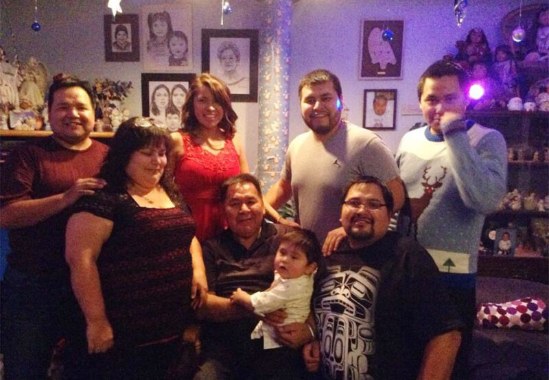 A group of eight people, including a young child, posing indoors with festive decorations and framed pictures in the background.