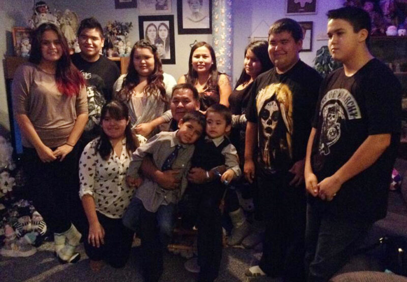 A group of people, including adults and children, smiling and posing inside a room decorated with framed pictures and various items.
